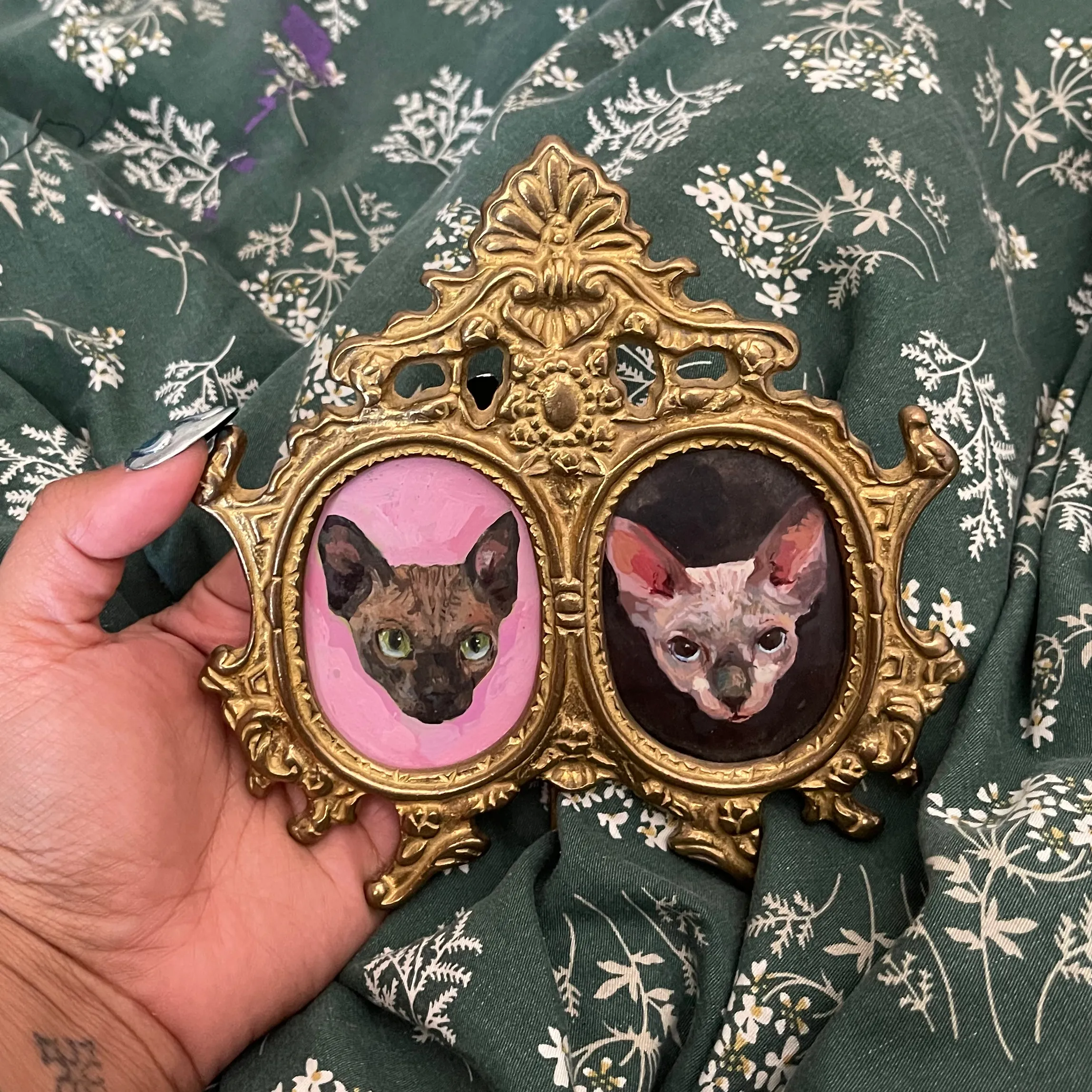 Two paintings, each of a hairless cat, set into a miniature frame.