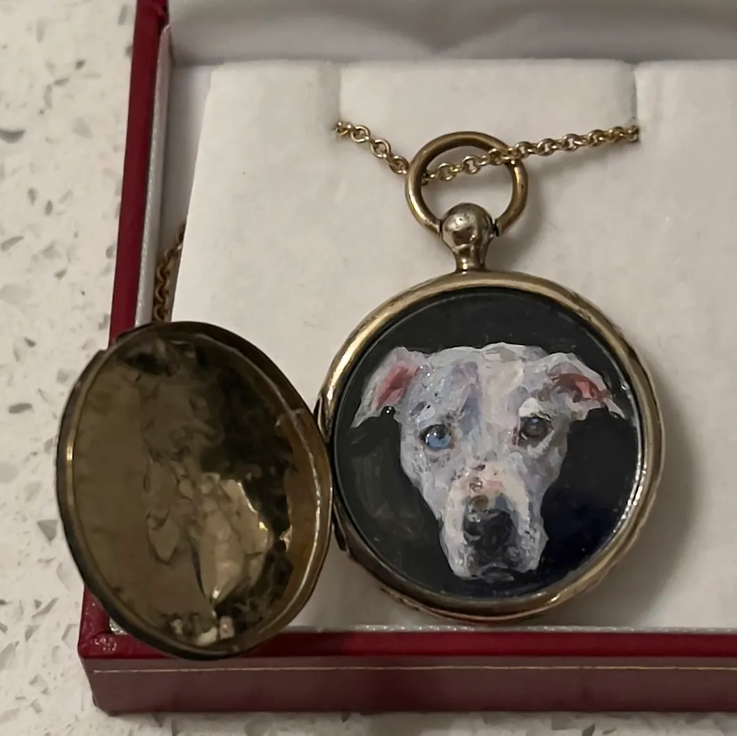 A painting of a white dog with one blue eye and one brown eye. The painting is set in an empty gold pocket watch.